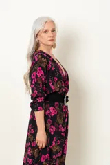 Vestido midi negro con estampado floral fucsia y marrón, escote en V cruzado, mangas largas y cinturón ancho negro con hebilla circular.