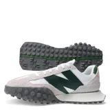 Championes urbanos New Balance, con capellada de gamuza color crema y detalles en blanco y verde. Presenta el logo "N" en cuero verde en los laterales y suela de goma texturizada en gris.
