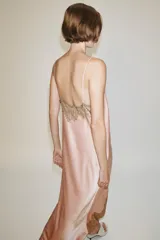 Vestido largo tipo lencero de Zara Woman Collection, confeccionado en tejido satinado color rosado con escote en pico y tirantes finos. Presenta detalles de aplicaciones de encaje a contraste y bajo asimétrico.