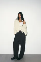 Pantalón de tiro alto con diseño tipo balloon, confeccionado en tejido con estampado de rayas verticales. Presenta pliegues frontales, bolsillos laterales ocultos y cierre frontal con cremallera, botón interior y ganchos metálicos.