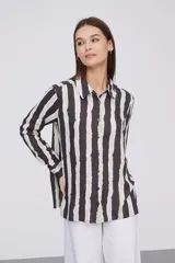 Camisa de manga larga con cuello clásico y cierre frontal de botones. Presenta un estampado de rayas verticales irregulares en tonos oscuros, blancos y verde claro.