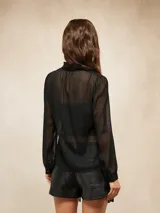 Camisa de tela semitransparente color negro con sutiles rayas verticales brillantes, cuello mao con volados, cierre frontal de botones y mangas largas con puños.