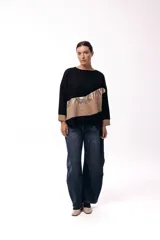 Sweater de punto con diseño de bloques de color en diagonal, combinando negro, beige y una franja central con textura metalizada. Presenta cuello redondo, mangas largas con puños en contraste y un corte holgado.