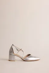 Zapato de tacón bajo color plateado, con punta fina, escote en V y tiras cruzadas en el empeine que se abrochan al tobillo. El tacón es ancho y mide 5 cm.