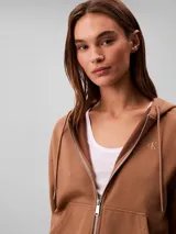 Campera canguro de felpa color marrón, con capucha ajustable con cordones, cierre frontal completo y bolsillos tipo canguro. Presenta el logo retro de Calvin Klein bordado en el pecho.