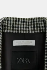 Blazer Zara de corte asimétrico confeccionado en tejido con lana. Presenta un diseño de cuadros, cuello con solapas de muesca, manga larga y cierre frontal cruzado con botones. El bajo es asimétrico con una abertura pronunciada en la espalda y cuenta con forro interior.
