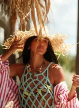 Sombrero de paja color beige con ala ancha y bordes deshilachados, decorado con una banda que incluye apliques de nácar.