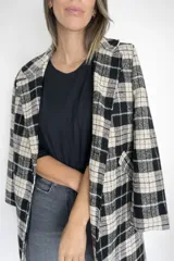 Chaqueta larga de corte sastrero con estampado de cuadros en tonos negro, blanco y detalles en beige. Presenta solapas clásicas, cierre frontal con botones y bolsillos laterales funcionales. Cuenta con forro interior y una estructura que aporta una caída elegante.
