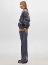 Pantalón jean de tiro alto y corte pinzado, con perneras de caída suelta y levemente anchas en el bajo. Posee pasador con hebilla en la parte trasera.