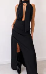 Vestido largo negro de fiesta, con escote halter pronunciado, detalle de cuello tipo choker con tiras colgantes y falda larga con abertura lateral.