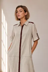 Vestido midi chemise de lino color beige, con cierre frontal de botones, cuello camisero, mangas cortas con vuelta y detalles en marrón oscuro en la botonera y los hombros.