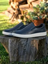 Zapatillas tipo slip-on de cuero azul marino con textura microperforada en la parte superior y suela de goma blanca.