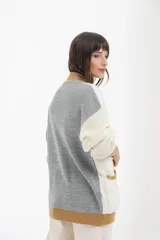 Cárdigan tejido de punto grueso, con diseño color block en gris, blanco y beige. Tiene cuello en V, cierre frontal con botones y un bolsillo de parche.
