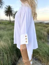 Camisola blanca de corte holgado con cuello alto y mangas largas con puños anchos abotonados.