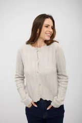 Saco de punto gris claro con textura acanalada, cuello redondo, cierre frontal con botones y bordes con terminación ondulada.