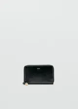 Billetera pequeña de poliuretano efecto charol color negro, con cierre perimetral y logo dorado impreso en el frente.