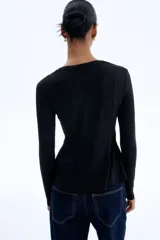 Top de manga larga confeccionado en punto de crepé, con cuello redondo y diseño de peplum. Presenta costuras moldeadoras en la parte frontal y posterior que definen la silueta.