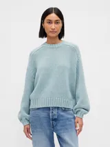 Buzo de punto con cuello redondo, mangas largas con puños ajustados y diseño holgado. Presenta un tejido de textura suave en color celeste.