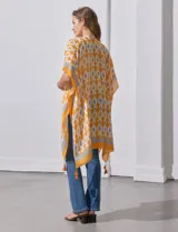 Kimono tejido con estampado abstracto en tonos azules, blancos y violetas. Tiene terminación de ruedo con borlas.