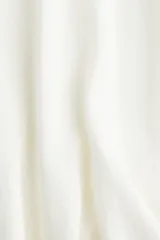 Top de punto fino color blanco, con cuello redondo acanalado, mangas cortas raglán y silueta acampanada tipo peplum en el bajo.