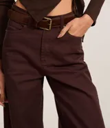 Pantalón wide leg de sarga color marrón oscuro, de talle alto con trabillas para cinturón, cierre de botón y cremallera, con bolsillos delanteros y traseros.