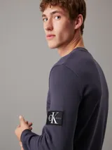 Remera de manga larga color gris de punto gofrado con cuello redondo y logo de Calvin Klein en la manga.