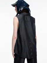 Camisa sin mangas en denim 100% lyocell, muy liviano con caída fluida. De corte recto y largo medio, presenta cartera escondida en el frente y un bolsillo plaqué en el pecho. En la espalda, un detalle distintivo: botones decorativos alineados en abertura vertical. Los pespuntes a contratono completan el look.