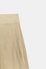 Bermuda de tiro alto color beige con trabillas en la cintura y detalle de pliegues en la parte delantera. Presenta un corte amplio y largo por debajo de las rodillas.