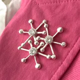Broche plateado con forma de dos copos de nieve superpuestos, con tres cristales incrustados.