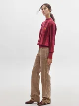 Pantalón de pana roja con corte holgado y tiro medio. Presenta una línea dorada a lo largo de la pierna.