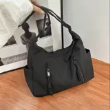 Bolso hobo negro de tela suave con múltiples bolsillos frontales con cierre y correa de hombro ajustable.