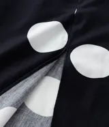 Vestido midi de algodón con estampado de lunares blancos sobre fondo negro. Presenta escote en V, mangas cortas abullonadas, cintura ajustada con cinturón de hebilla y falda con tajo lateral.