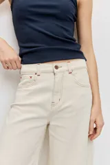 Pantalón denim de corte wide leg, tiro alto y color crudo con costuras en contraste.