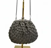 Bolso de mano tejido artesanalmente en hilo gris con detalles de canutillos en tono peltre. Presenta una boquilla metálica estilo vintage con cierre a presión y una cadena larga plateada para llevar al hombro.