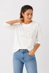 Remera de algodón color blanco con mangas 3/4 y cuello redondo. Presenta un diseño frontal con bordado en broderie, detalles de strass y la inscripción 'Rose Blanche'.