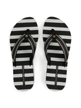 Ojotas de mujer con plataforma tipo cuña, suela EVA dentada y tiras de textil trenzado a rayas negras y blancas. Presentan una insignia con monograma TH en la tira del dedo.