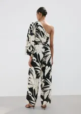 Mono largo de viscosa con diseño bicolor en negro y beige con estampado de hojas tropicales. Presenta un corte asimétrico de un solo hombro con manga larga holgada, pantalón de silueta recta y lazo ajustable en la cintura.