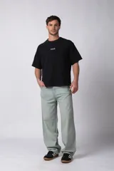 Remera de corte boxy y fit cuadrado, confeccionada en algodón grueso de alta calidad. Presenta un diseño minimalista en el frente con un pequeño logo circular y una estampa de gran tamaño en la espalda con la frase 'Designed in South America, Worldwide Clothes'.