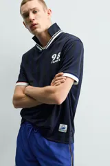 Polo de corte relajado confeccionado en tejido técnico, con diseño de rayas verticales en tonos azul marino y negro. Presenta cuello solapa con abertura frontal y detalles de rib en contraste en cuello y mangas. Incluye estampado frontal con el número 98 y la inscripción France, además de una etiqueta aplicada en el ruedo inferior.