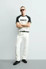 Camiseta de corte regular con diseño color block, cuerpo en color blanco y mangas ranglán en color negro. Presenta cuello redondo, detalles de rib a contraste en los puños y estampado frontal con la leyenda Mexico 70.