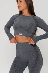 Conjunto deportivo de dos piezas compuesto por un top de manga larga tipo crop top con aberturas para pulgares y una calza de tiro alto. Ambas prendas presentan un diseño seamless con detalles de texturas perforadas y el logo de la marca estampado en el frente.