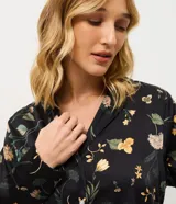 Pijama de dos piezas confeccionado en satén con estampado floral sobre fondo negro. La blusa es estilo camisa con cuello solapa, manga larga y cierre frontal con botones. El pantalón cuenta con cintura elástica y corte recto.