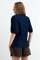 Blusa de denim oscuro con cuello en V, cierre frontal de botones y mangas cortas abullonadas con puños elastizados.