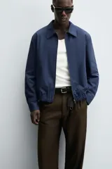 Cazadora regular fit color beige, confeccionada en tejido de algodón. Cuenta con cuello solapa, manga larga con puño elástico y trabilla, bolsillos de vivo en la cadera, bajo elástico y cierre frontal con cremallera.