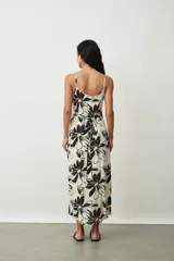 Vestido midi de tirantes finos, con escote en V y diseño cruzado estilo pareo. Presenta un estampado floral grande en tonos negros y naranjas sobre base off-white.