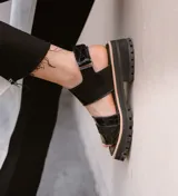 Sandalias de cuero color crudo con dos tiras horizontales en el empeine, una de cuero liso y otra con detalle dorado. Suela track color beige.