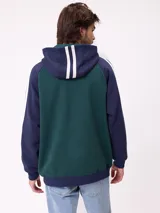 Canguro con capucha de estilo deportivo, con cuerpo en color celeste y mangas raglán en color negro. Presenta el logo de la marca estampado en el pecho, bolsillo tipo canguro frontal y franjas blancas laterales en las mangas.