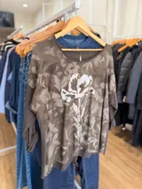 Remera de línea italiana con estampado floral en tonos marrones y detalle de flor central con letras doradas. Posee cuello redondo, mangas tres cuartos y cordón ajustable en el ruedo.