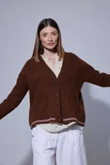 Saco tejido en lambswool con diseño de rombos y trenzas en el frente. Presenta cierre frontal con botones, cuello en V y detalles de rayas en contratono en puños y ruedo. Incluye pin bordado en la manga.