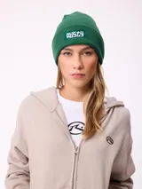 Gorro tipo beanie de tejido de punto acanalado en color marrón, con parche rectangular frontal con el logo de la marca Rusty.